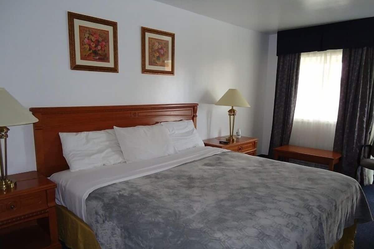 A hotel room with a large bed, two bedside tables, a nightstand, a lamp, and two framed pictures on the wall.