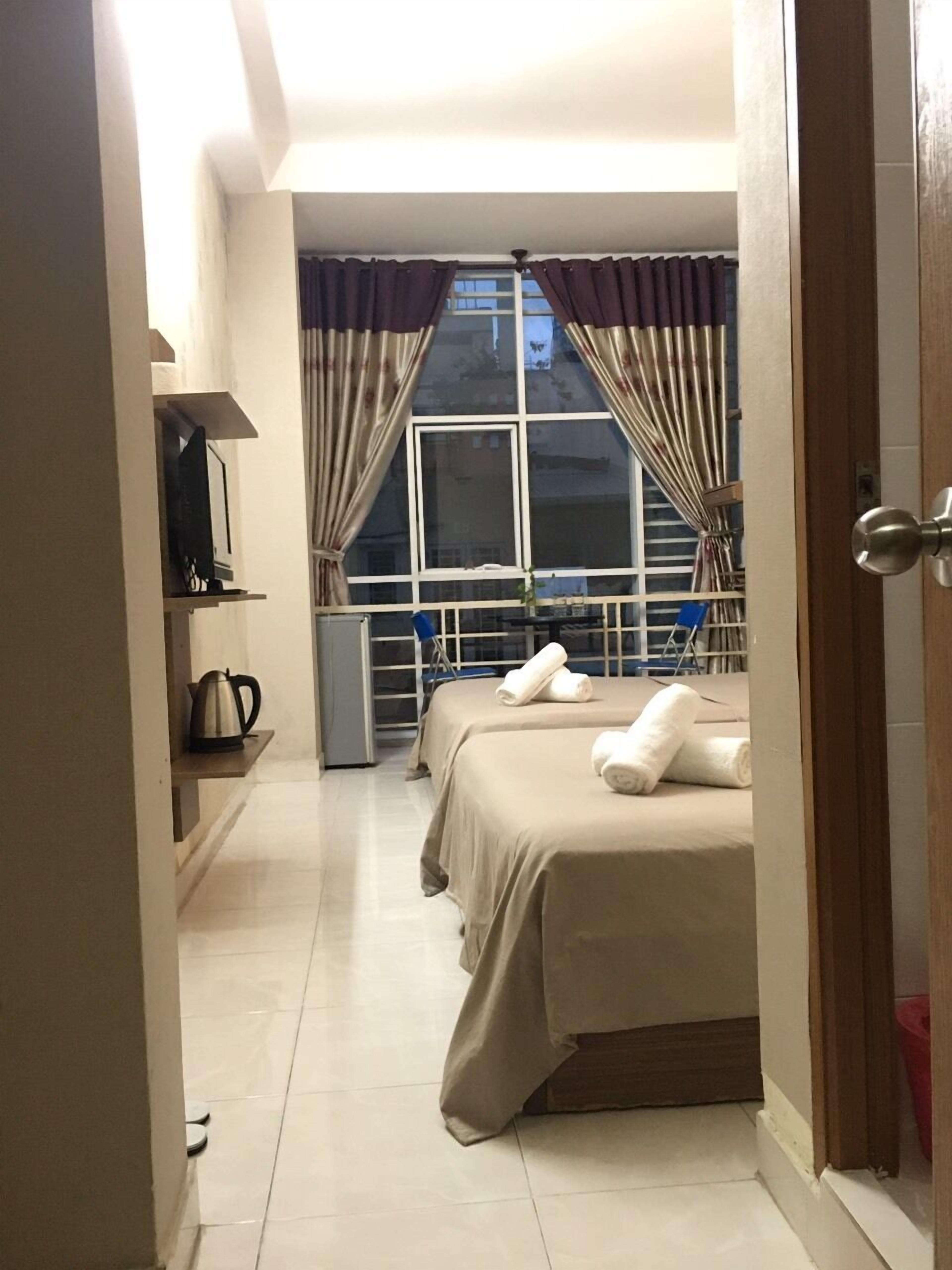 Una habitación de hotel con dos camas, un televisor en un estante y una ventana con cortinas.