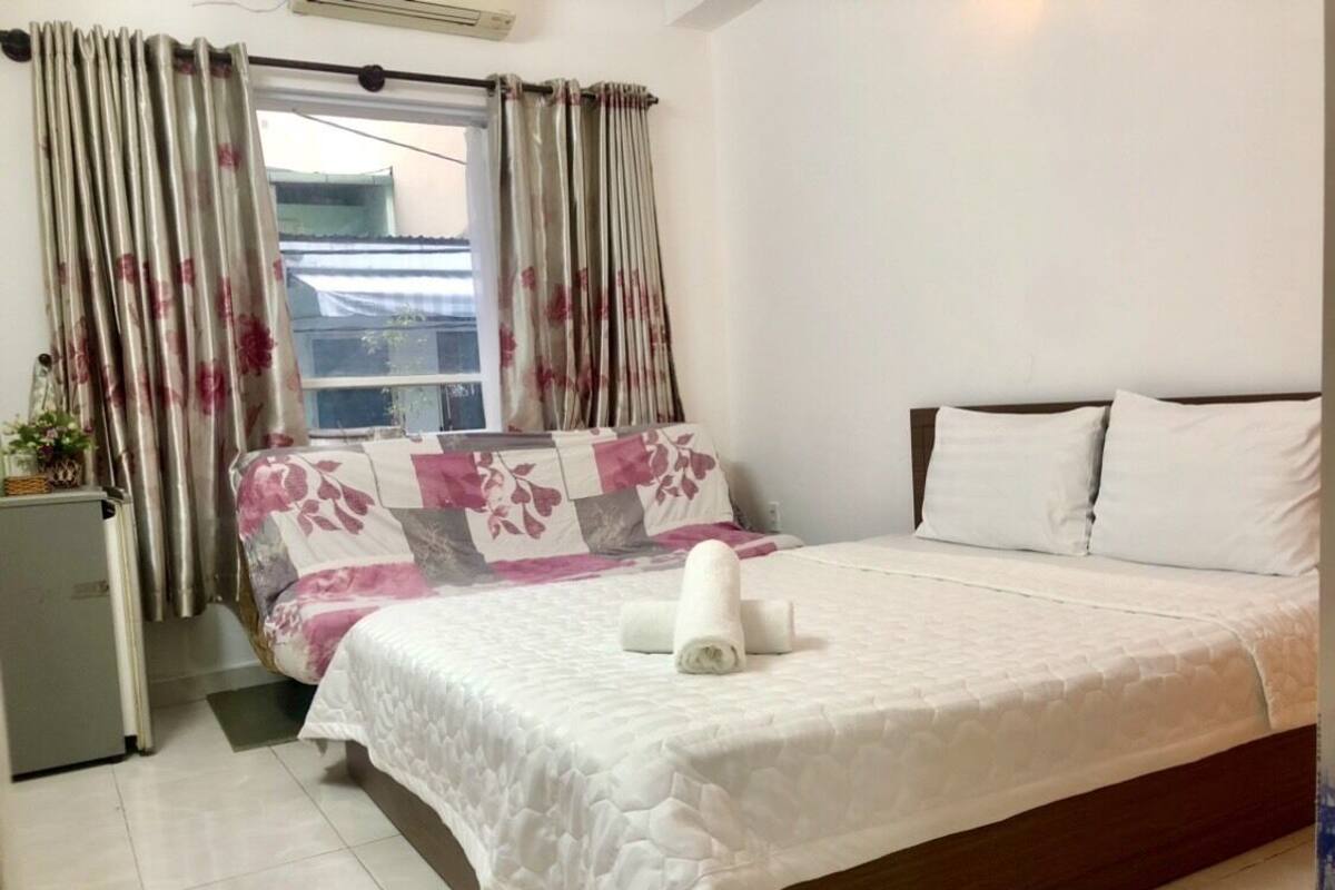 Une chambre à coucher avec un lit, un petit réfrigérateur et une fenêtre avec des rideaux.