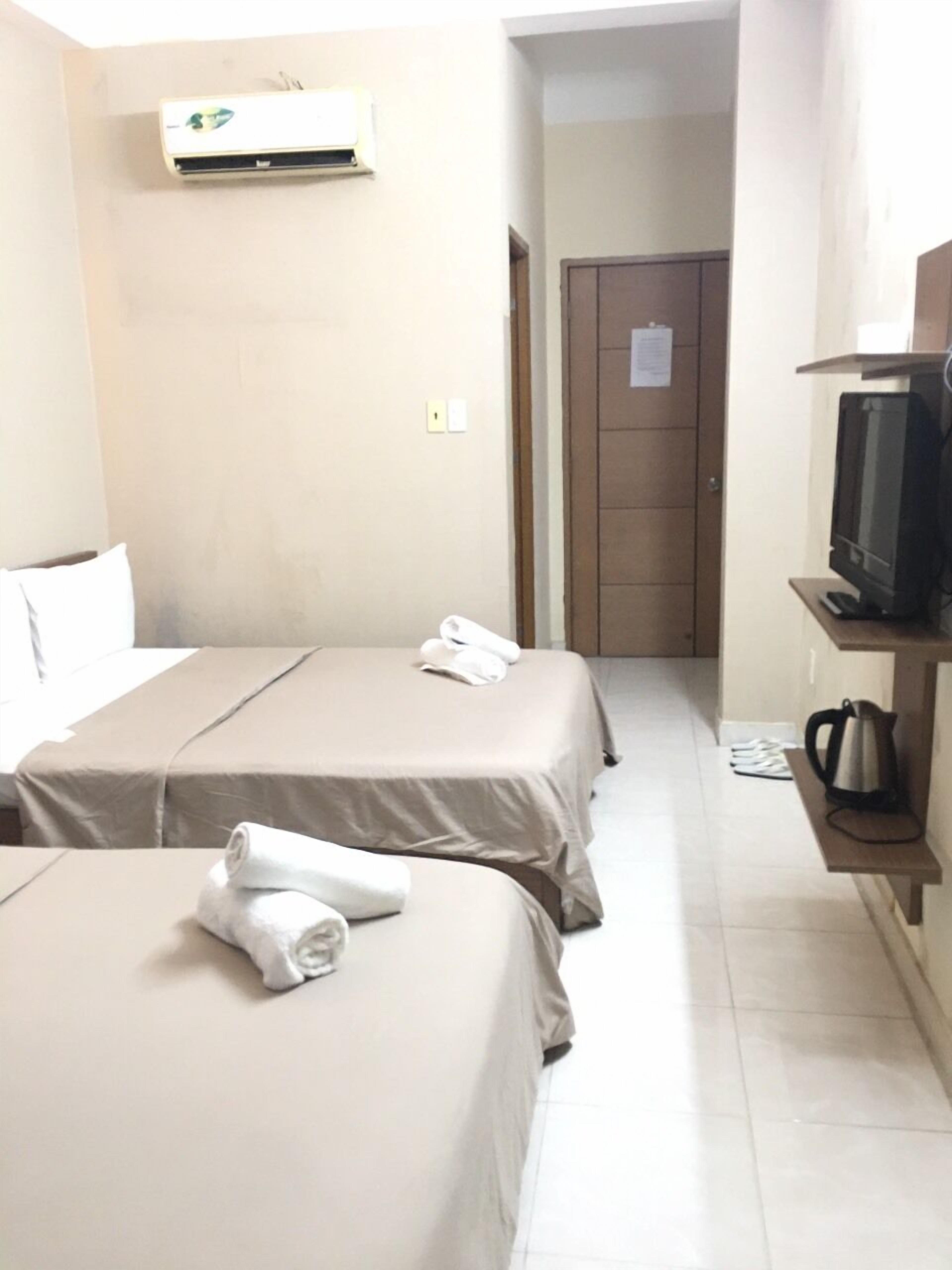 A hotel room with two beds, a television on a stand, and an air conditioning unit on the wall.