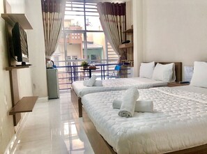 A hotel room with two beds, a balcony with a table and chairs, and a view of buildings outside. - Thanh Ha Guesthouse (Ho Chi Minh City)
