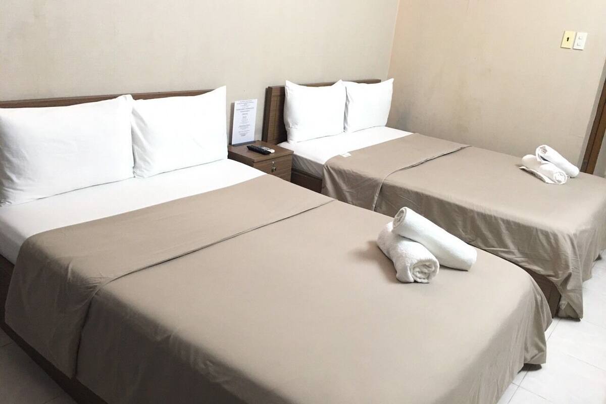 Une chambre d’hôtel avec deux lits simples, chacun recouvert d’une couvre-lit beige et agrémenté d’oreillers blancs. On y trouve deux tables de chevet avec des lampes, ainsi qu’une petite table sur laquelle repose une télécommande.