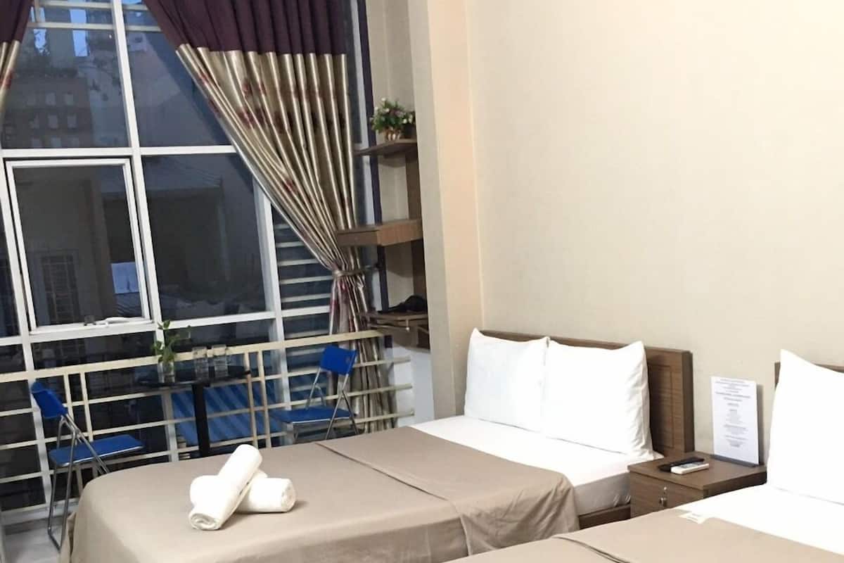 Une chambre d’hôtel avec deux lits, une fenêtre avec des rideaux, une petite table et une chaise.