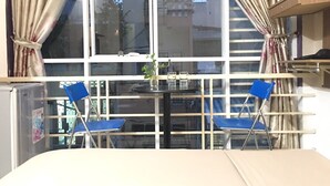 Ein Zimmer mit einem großen Fenster, zwei blauen Stühlen, einem kleinen Tisch mit einer Vase und Gläsern sowie einem Kühlschrank.