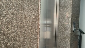 Ein moderner Aufzug mit Metalloptik neben einer Wand mit Granitstruktur.