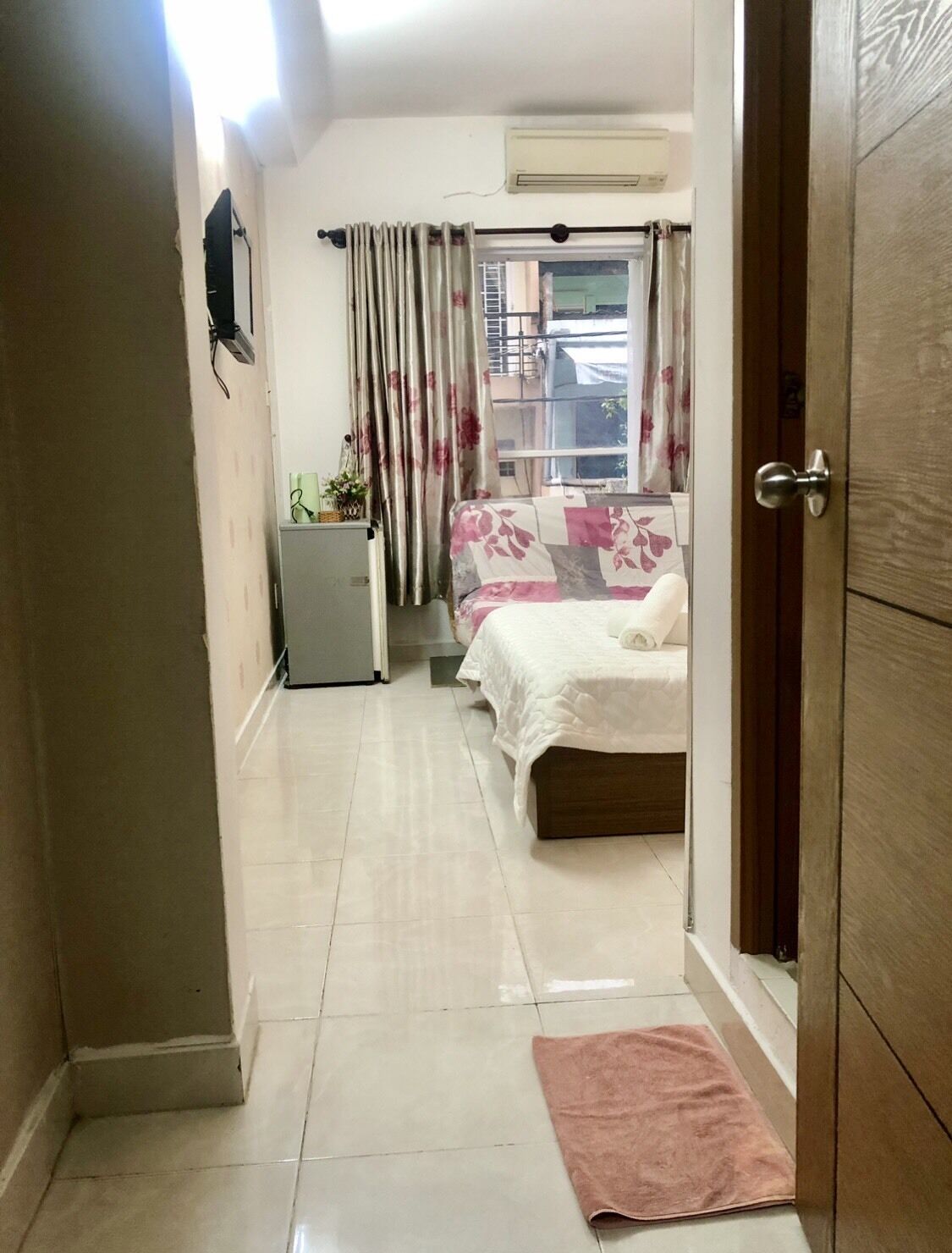 A bedroom with a bed, a small table, a radiator, and a window with curtains.
