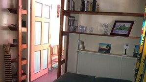 A room with a bed, a wooden chair, a bookshelf, and a door leading to another room. - Italian Guesthouse (Gros Islet)