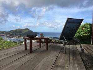 Eine Holzterrasse mit Tisch und Stuhl mit Blick auf einen Yachthafen und sanfte Hügel in der Ferne.