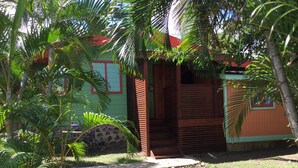 A small, rustic wooden house with a green exterior and a red roof, surrounded by lush tropical vegetation. - Italian Guesthouse (Gros Islet)