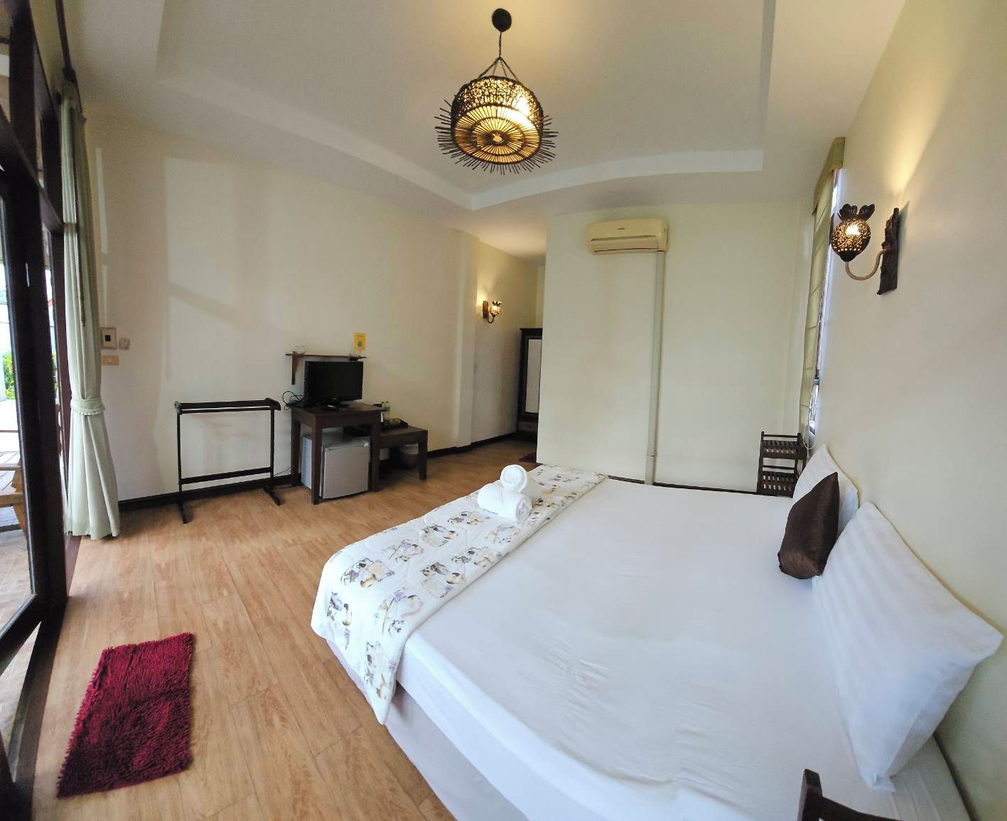 Une chambre d’hôtel comprenant un lit, un bureau avec une télévision, un appareil de climatisation et une fenêtre avec des rideaux.