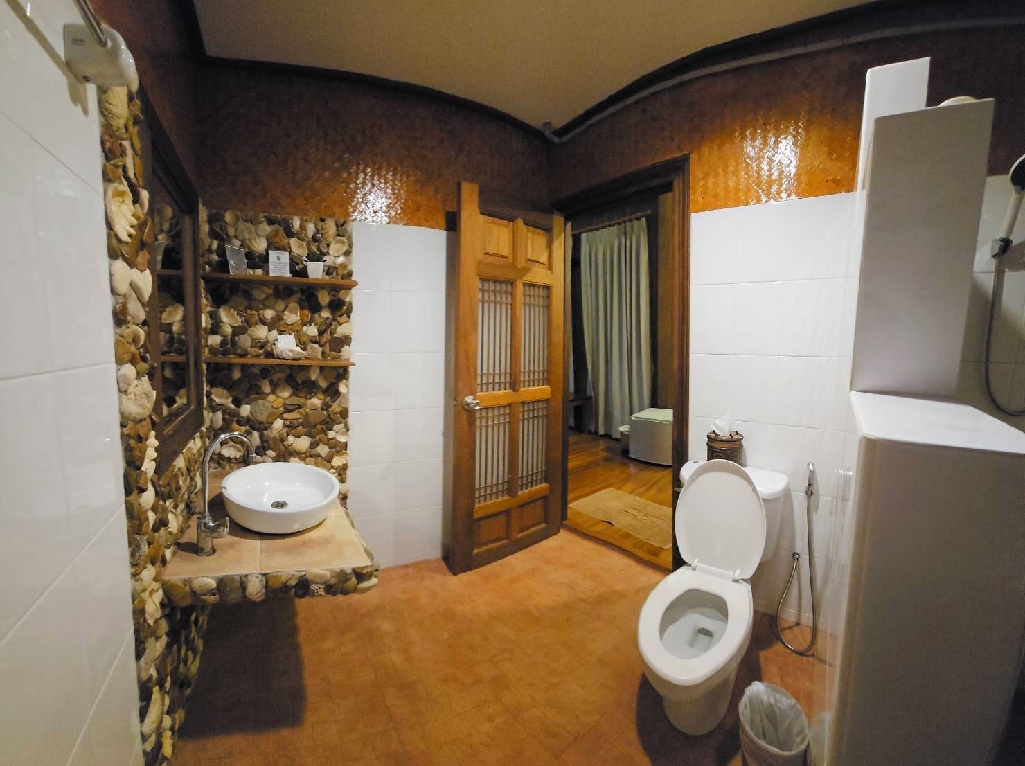 Un baño con pared de piedra, lavamanos, inodoro y zona de ducha.
