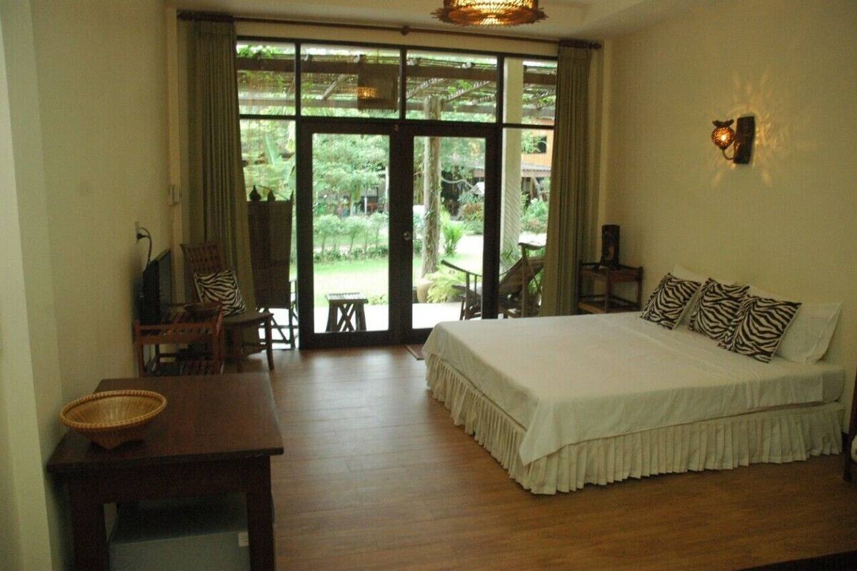 Ein Schlafzimmer mit einem großen Bett, einem Esstisch und Blick auf einen Garten durch eine Glastür.