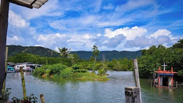 A riverside view with a wooden structure, a small dock, and a houseboat in the background.