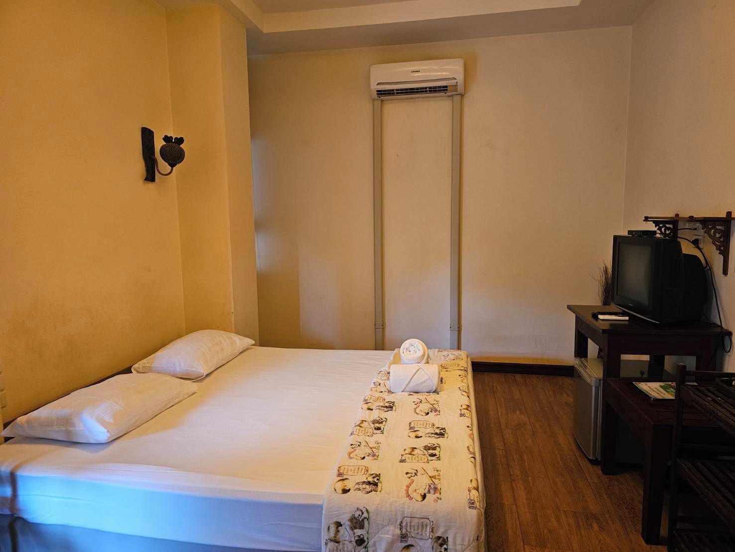 A hotel room with a bed, a television, and an air conditioning unit.