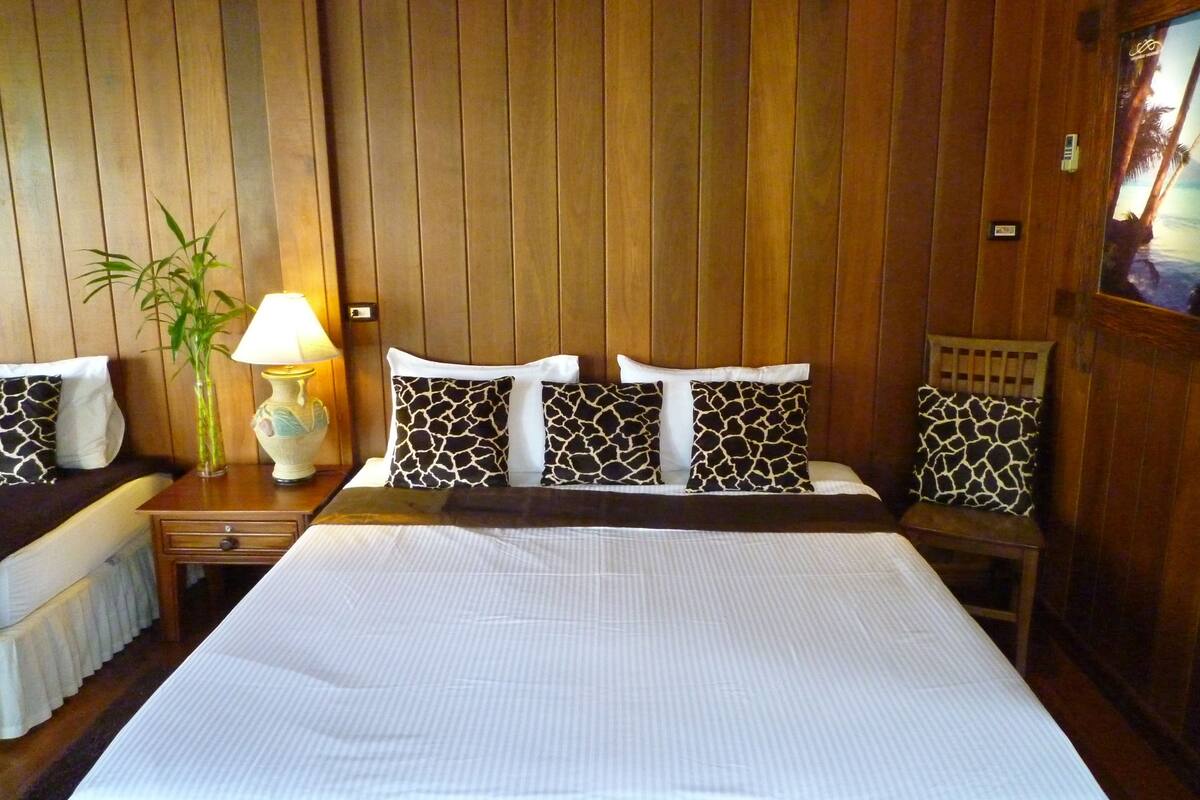 Ein Hotelzimmer mit einem großen Bett, Holzwandverkleidung, einem Nachttisch mit Lampe und einer Pflanze.