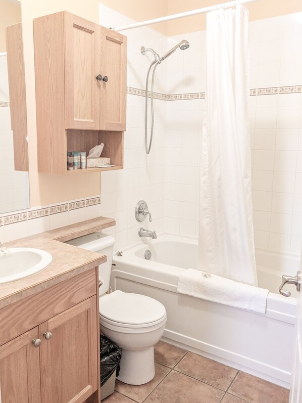 Une salle de bain avec un meuble-lavabo en bois, des toilettes, une baignoire et un rideau de douche.