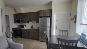 A compact kitchen with dark wooden cabinets, stainless steel appliances, and a dining area with a table and chairs. - Desert Surfside Waterfront Accommodations (Osoyoos)
