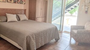 A bedroom with a bed, a wooden wardrobe, a chair, and a sliding glass door leading to a balcony. - Desert Surfside Waterfront Accommodations (Osoyoos)