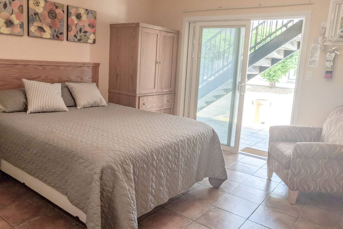 A bedroom with a bed, a wooden wardrobe, a chair, and a sliding glass door leading to a balcony.