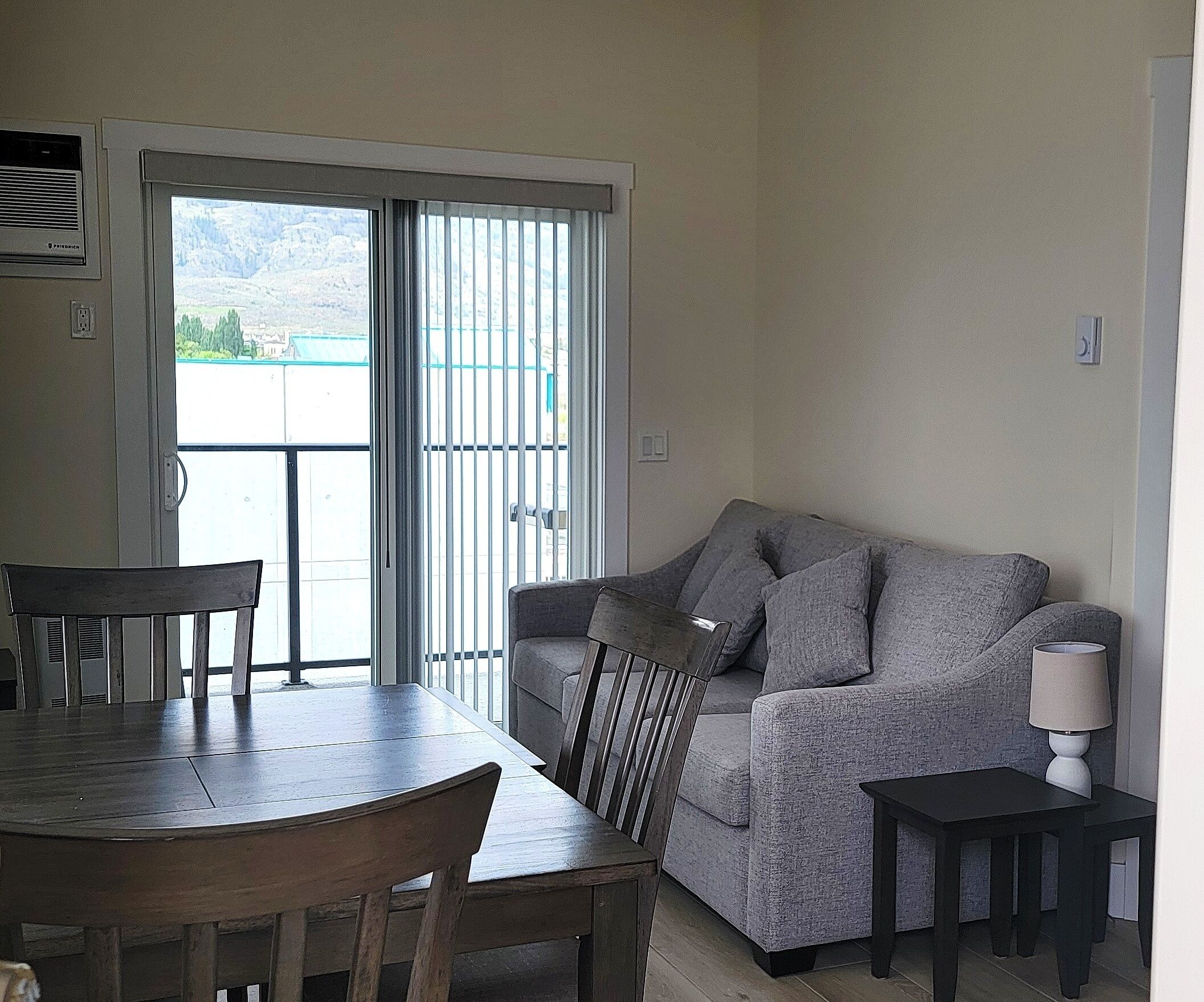 A living room with a grey sofa, a wooden dining table, and a lamp.