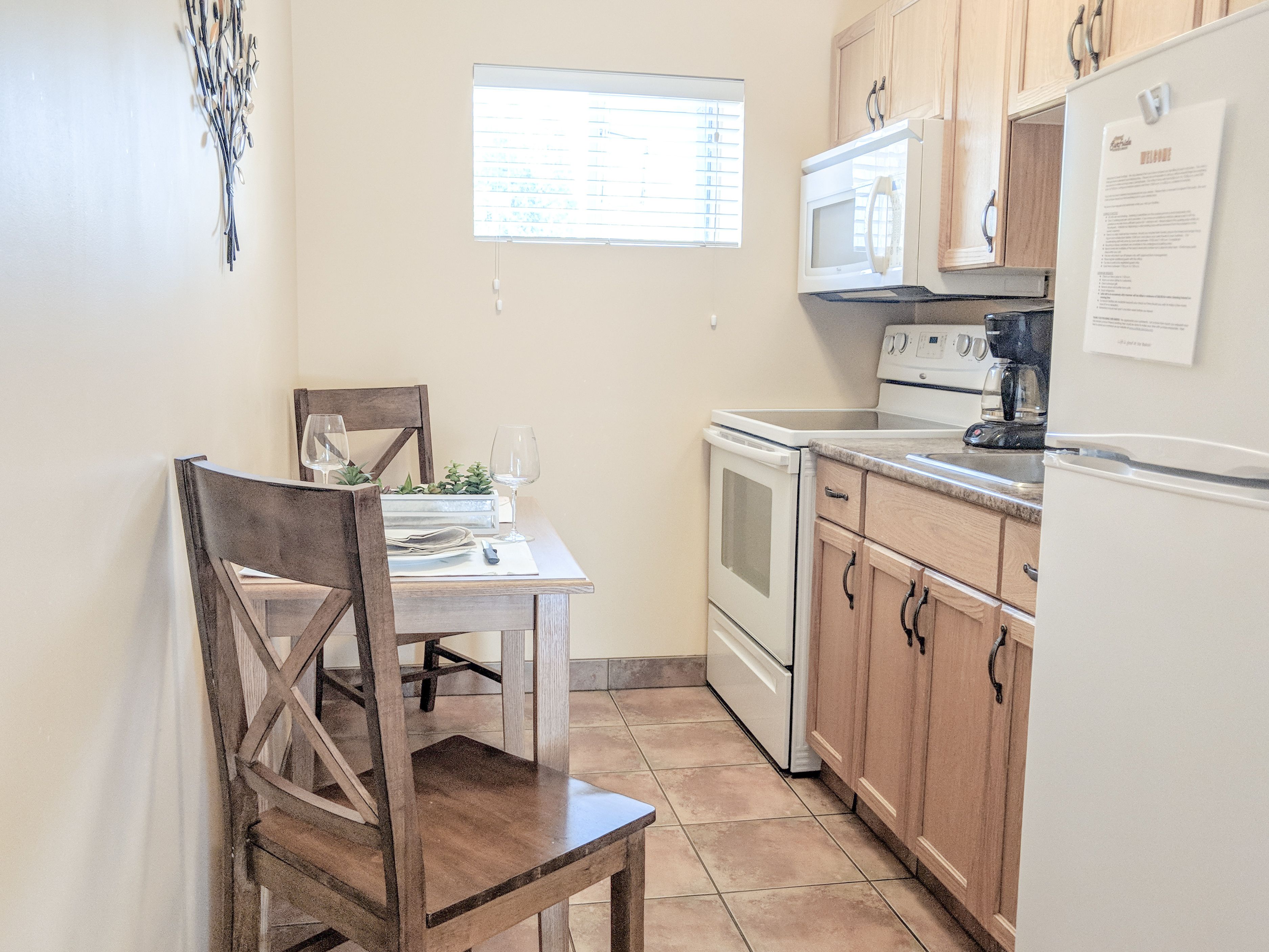 Une cuisine compacte comprenant une table à manger, des chaises en bois, un four à micro-ondes, une cuisinière et des placards.