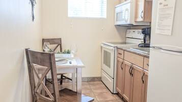 Une cuisine compacte comprenant une table à manger, des chaises en bois, un four à micro-ondes, une cuisinière et des placards.