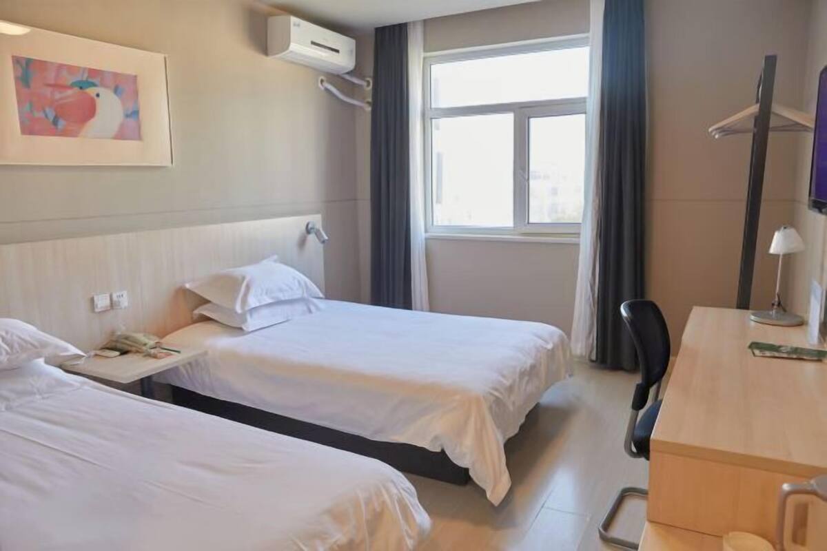 Une chambre d’hôtel avec deux lits, un bureau, une chaise, une fenêtre avec des rideaux et un tableau au mur.