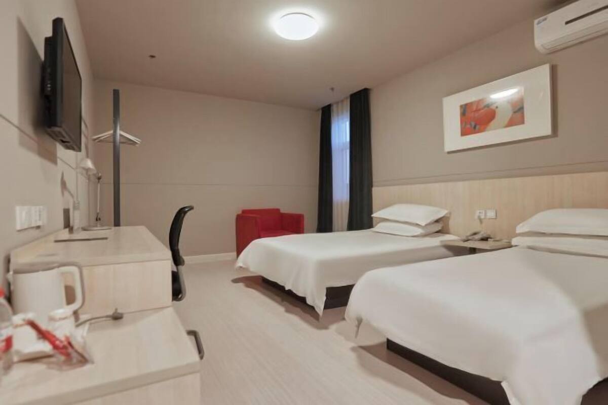 Une chambre d’hôtel avec deux lits, un bureau doté d’une machine à café, une télévision et un fauteuil rouge.