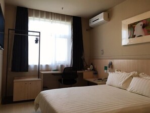 A hotel room with a bed, a desk, a chair, a wardrobe, a window with curtains, and an air conditioning unit. - Jinjiang Inn Langfang High-Speed Rail Station Yinhe South Road (Langfang)