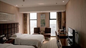 Quarto de hotel com duas camas, uma escrivaninha com televisão, uma cadeira e uma janela com cortinas.
