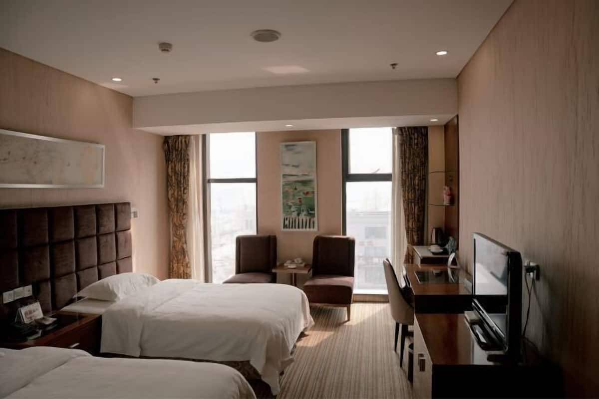 A hotel room with two beds, a desk with a TV, a chair, and a window with curtains.
