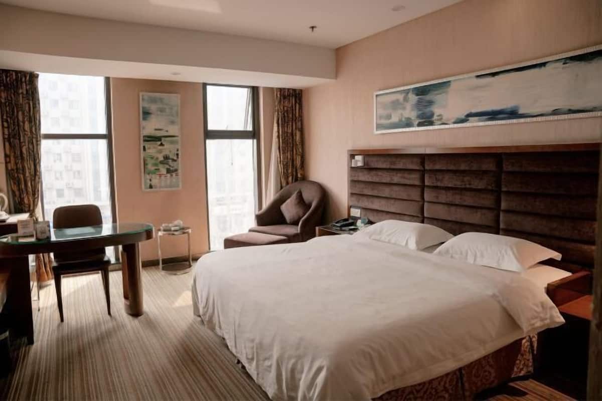 A hotel room with a large bed, a desk, a chair, and a painting on the wall.