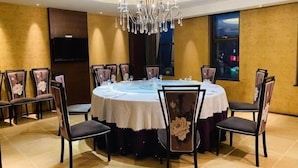 Uma sala de conferências com uma mesa redonda, cadeiras, um lustre, uma televisão de tela plana e uma janela com vista para a cidade.