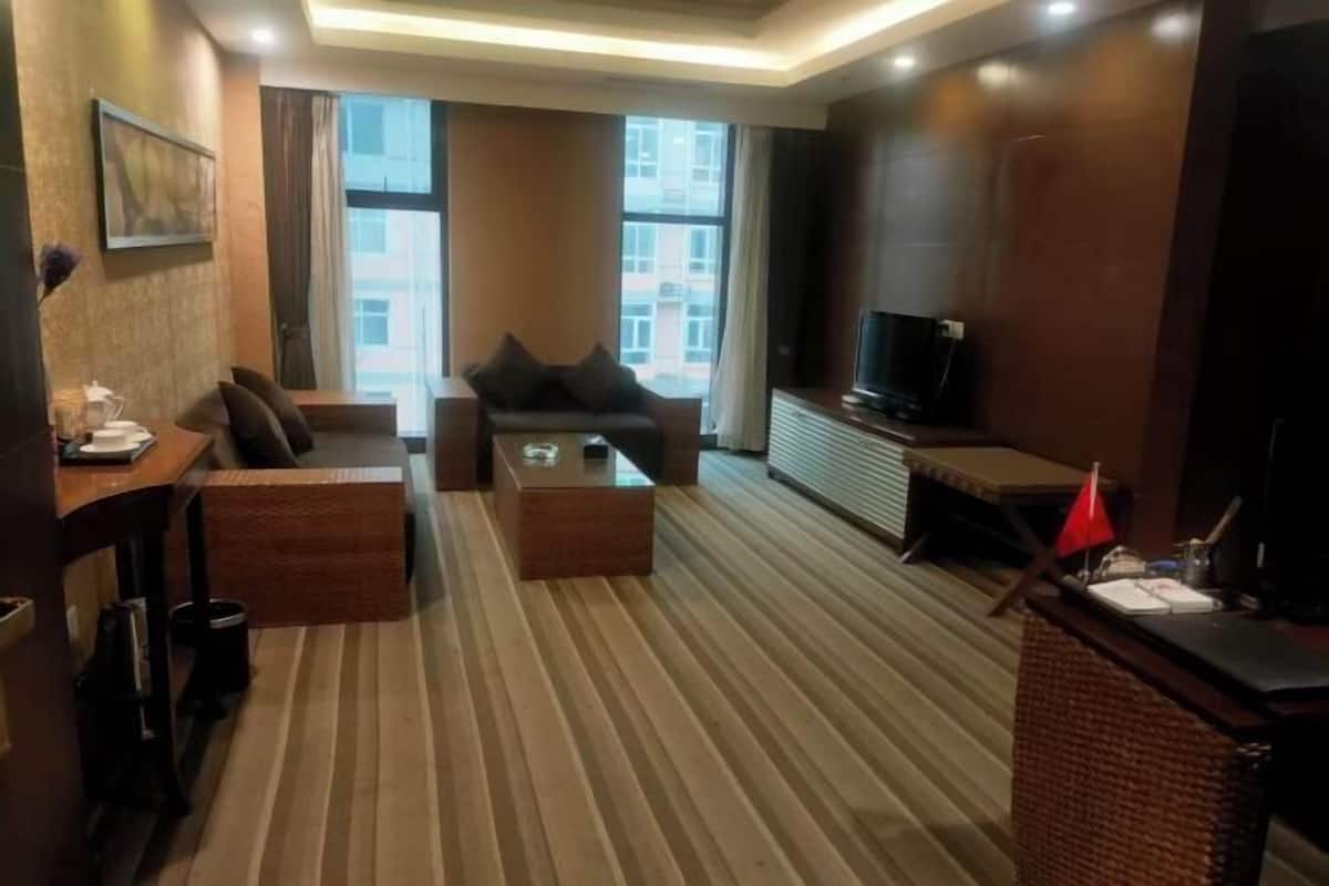 A hotel room with a sofa, a coffee table, a TV, and a small table with a lamp.