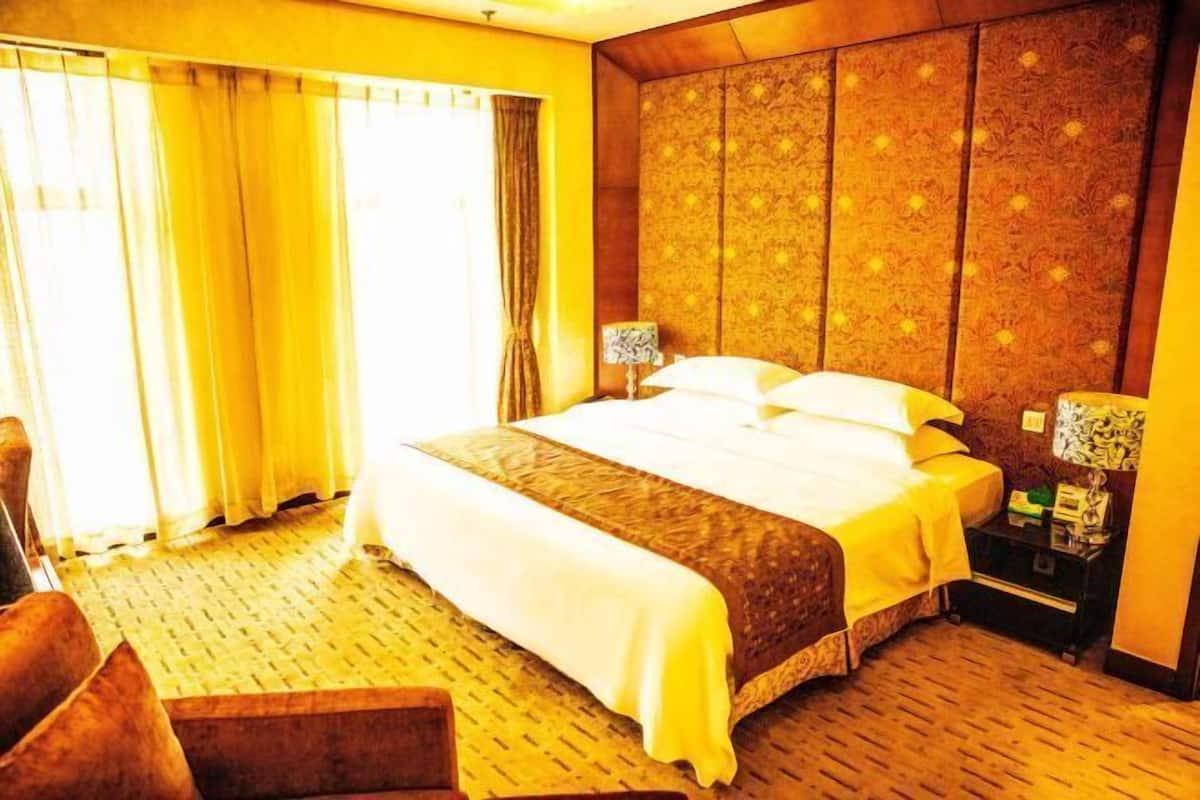 A hotel room with a large bed, a wooden headboard, a nightstand, and a chair.