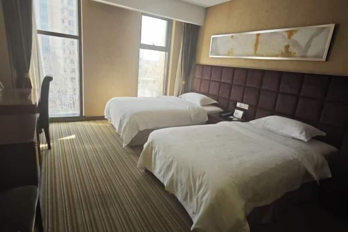 A hotel room with two beds, a desk, and a large window.