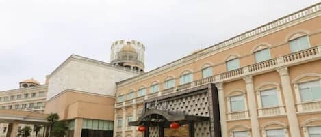 A hotel entrance with a large archway, a tower, and a parking area.
