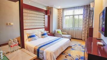 Quarto de hotel com uma cama grande, uma escrivaninha com cadeira, uma televisão e uma janela com cortinas.