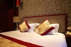 Una cama bien tendida con almohadas blancas y rojas, un cabecero de madera y un papel tapiz estampado.
