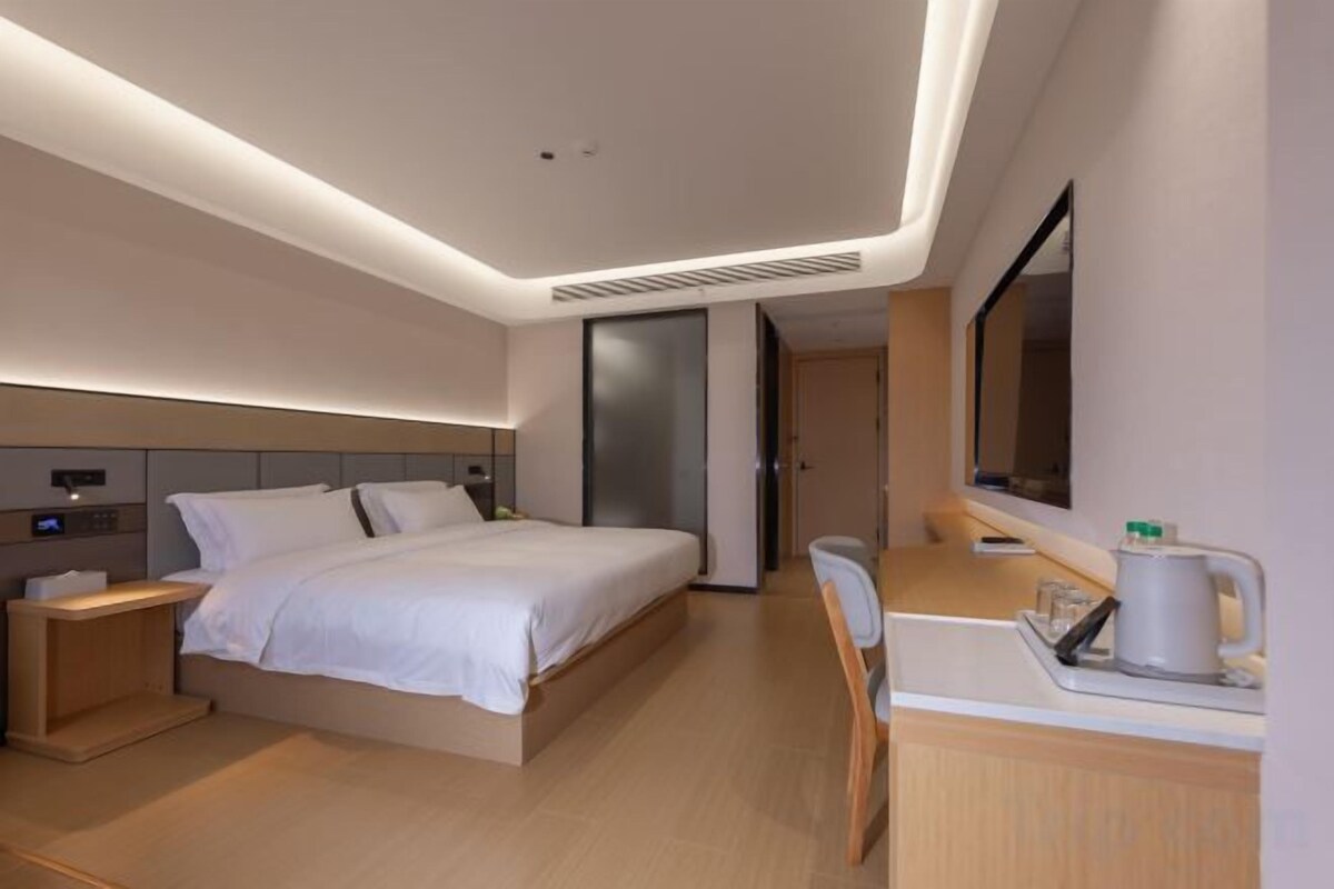Habitació d'hotel moderna amb llit, taula de nit, escriptori, cadira i un mirall gran.