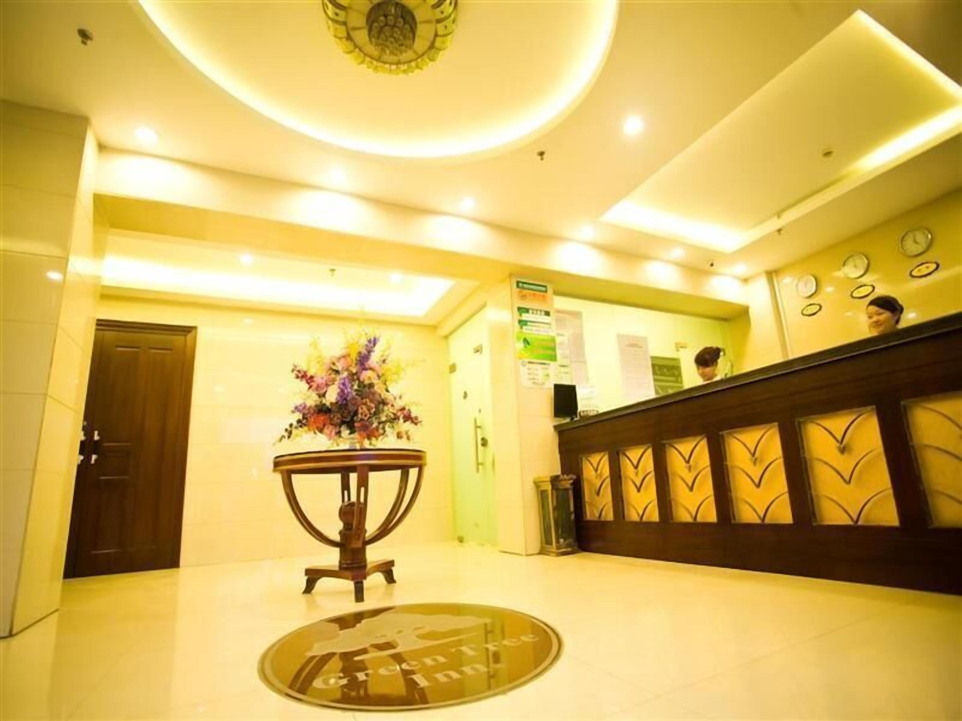 A hotel lobby with a reception desk, a floral centerpiece, and a circular logo on the floor.