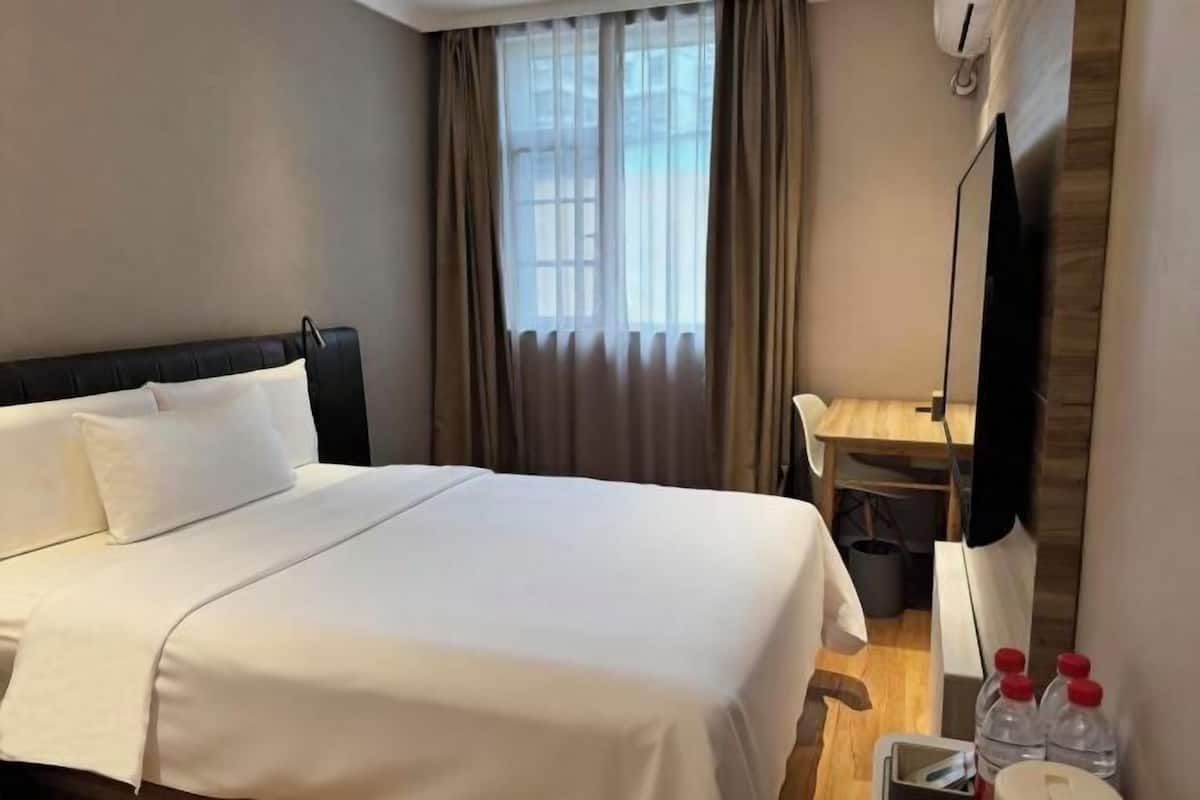 A hotel room with a bed, a desk, a chair, a TV, and a window with curtains.