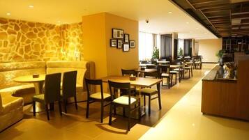 Un hall de hotel con pared de piedra, una recepción y varias mesas y sillas para comer.