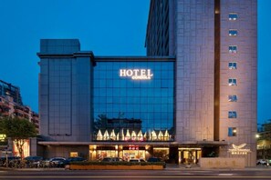 Ein Hotelgebäude mit einem auffälligen 'HOTEL'-Schild, einer großen Glasfassade und einem Parkplatz davor.