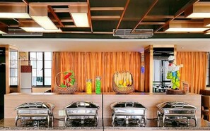 Un buffet avec plusieurs points de service, un mur décoratif agrémenté de rideaux et une statue de chef cuisinier.