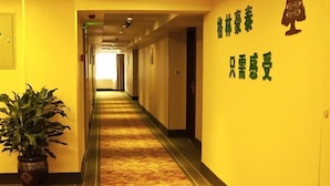 A hotel hallway with a carpeted floor, a potted plant, and a wall with green text and a tree silhouette. - Greentree Inn Nantong Stadium West Qingnian Road Business Hotel (Nantong)