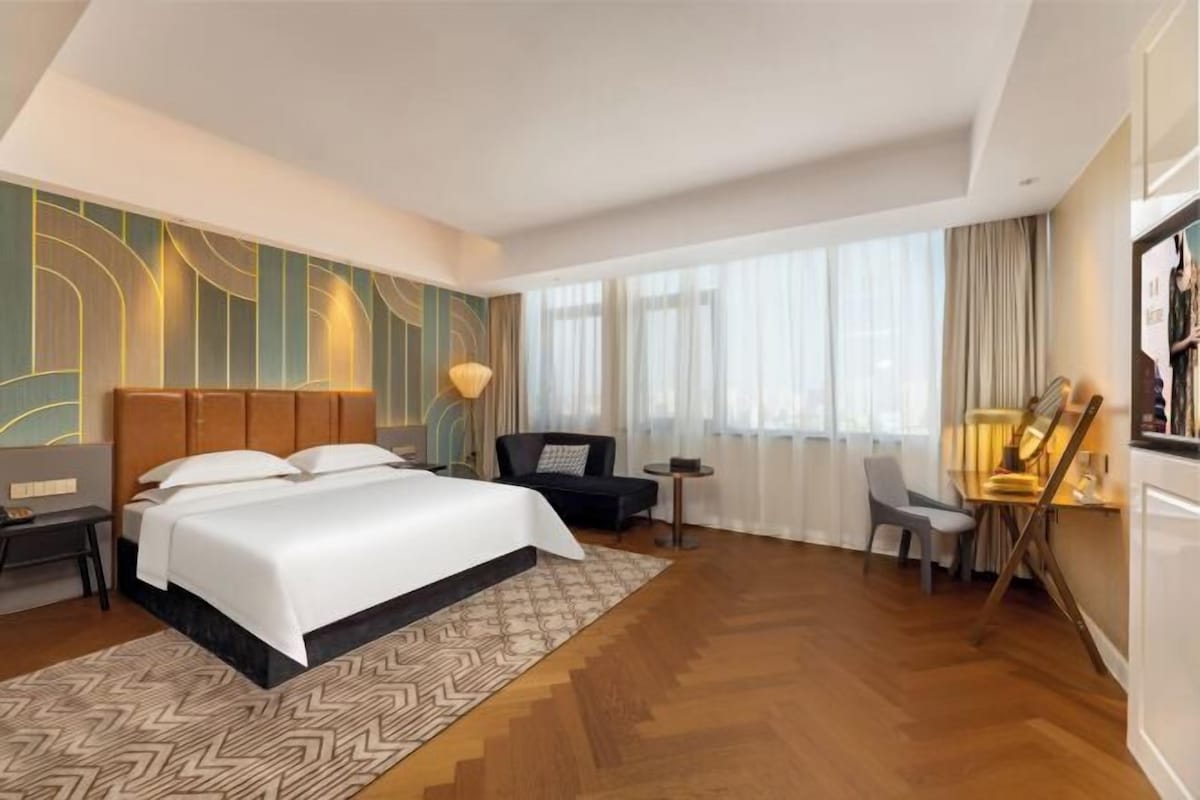 Une chambre d’hôtel avec un grand lit, un bureau, une chaise et une fenêtre avec des rideaux.