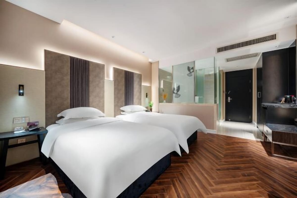Une chambre d’hôtel moderne avec deux lits, un grand miroir, un parquet en bois disposé en chevrons et un petit bureau avec un téléphone.
