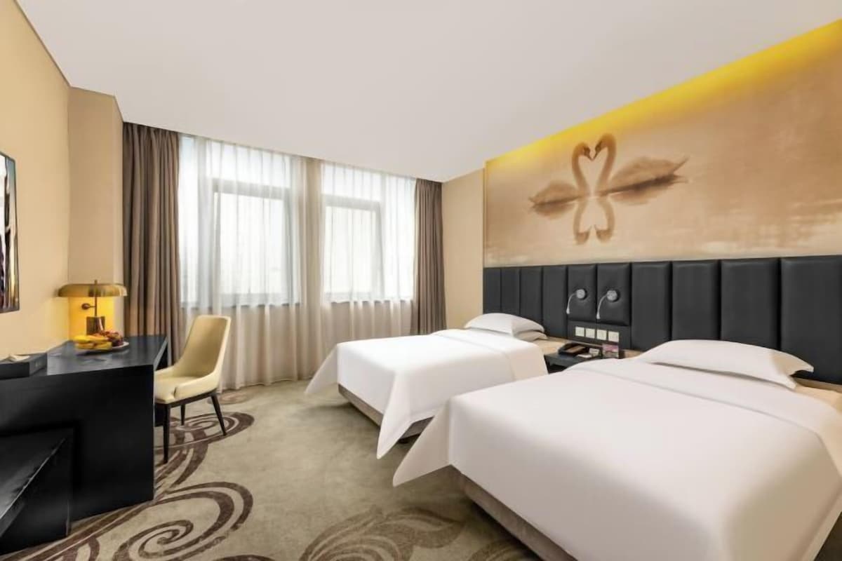 Une chambre d’hôtel avec deux lits, un bureau, une chaise et une grande fenêtre avec des rideaux.