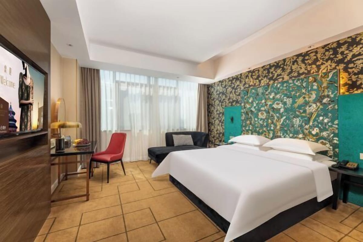 Une chambre d’hôtel avec un grand lit, un bureau, une chaise rouge, un canapé noir et un téléviseur fixé au mur.